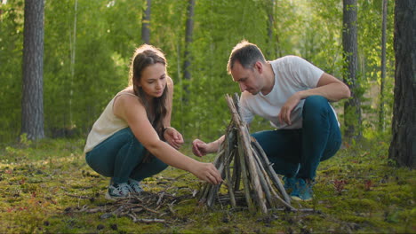 A-couple-man-and-a-woman-together-collect-a-fire-from-sticks-in-the-woods.-A-young-couple-in-a-hike-puts-a-fire-for-the-night-and-cooking-in-nature